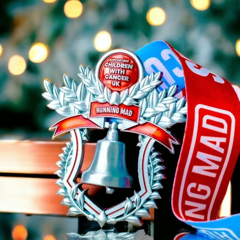 Festive charity medal supporting Children with Cancer UK on a wooden surface.