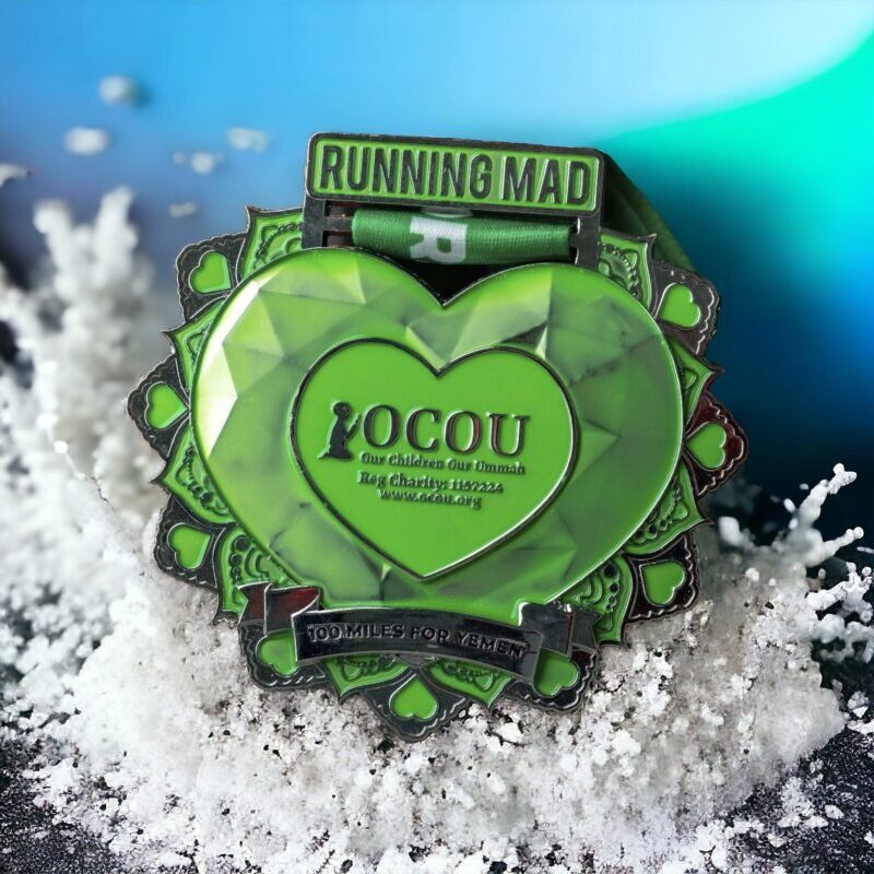 Green heart-shaped Running Mad medal for OCOU 100 Miles for Yemen, displayed on a snowy backdrop.